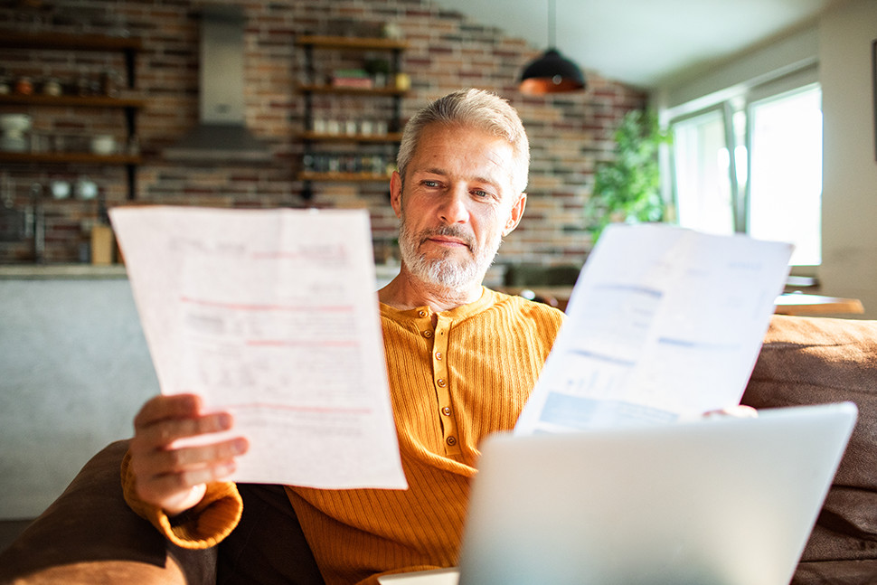 Homeowner sitting on a couch comparing two different window replacement cost estimates on paper documents.