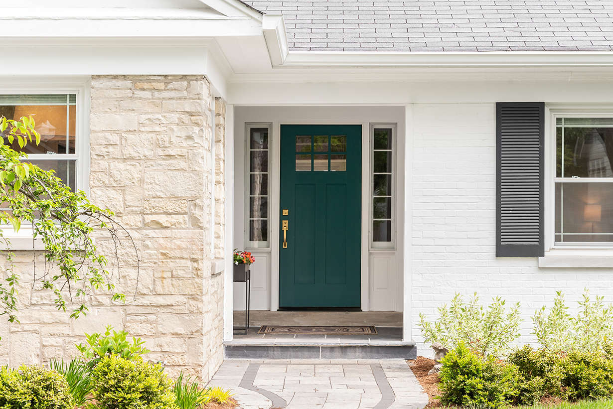 Exterior view of a renovated British Columbia home featuring a dark green front entry door flanked by modern double-hung windows.