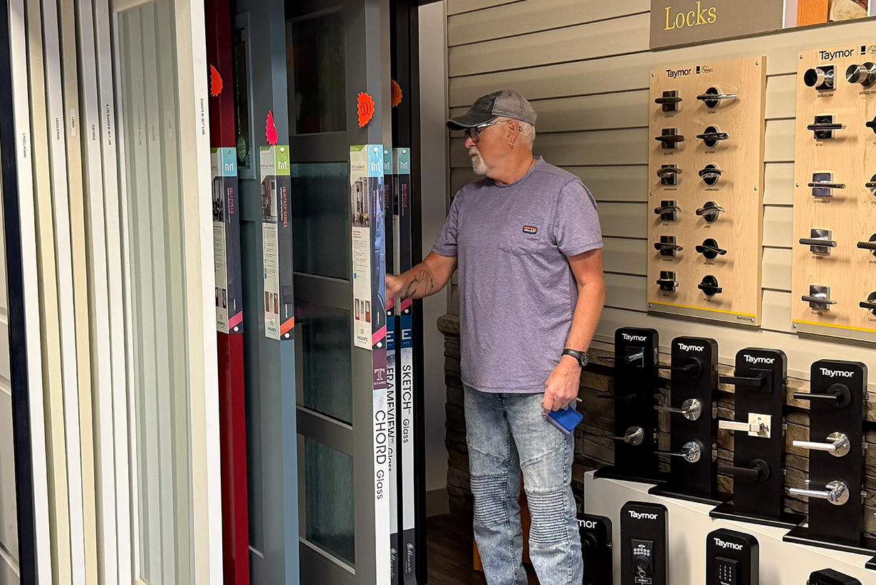 Customer browsing door glass options and hardware displays in a door replacement showroom.